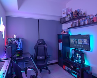 A modern gaming setup featuring a sleek gaming chair, dual monitors on a desk, and LED lighting. A gaming console and various decorations are displayed on shelves, creating an organized and vibrant gaming environment.