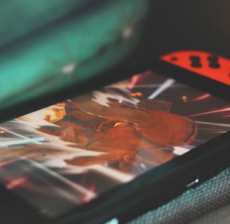 A portable gaming console with neon red and blue controllers displays an action-packed scene from a video game. The screen is focused on a character surrounded by bright, dynamic light effects.
